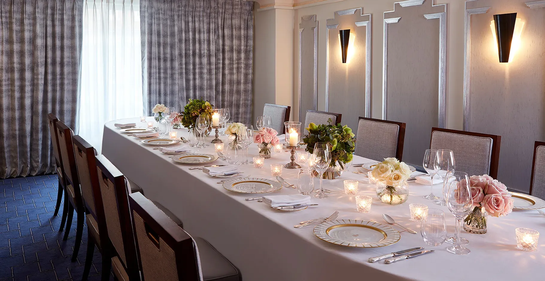 The Clarence Room at Claridge’s prepared for an intimate dinner with a long table dressed in white linen, floral arrangements, candlelight, and elegant place settings.