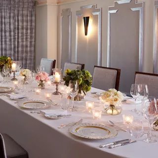 The Clarence Room at Claridge’s prepared for an intimate dinner with a long table dressed in white linen, floral arrangements, candlelight, and elegant place settings.