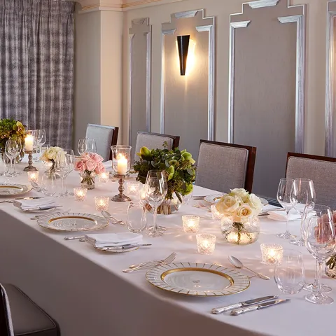 The Clarence Room at Claridge’s prepared for an intimate dinner with a long table dressed in white linen, floral arrangements, candlelight, and elegant place settings.