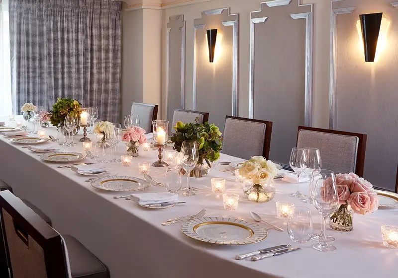 The Clarence Room at Claridge’s prepared for an intimate dinner with a long table dressed in white linen, floral arrangements, candlelight, and elegant place settings.