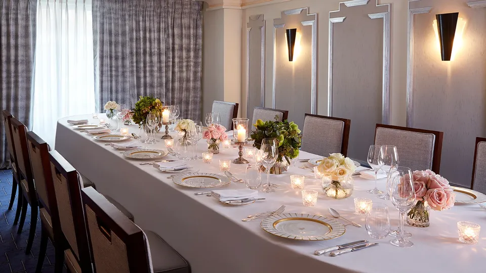 The Clarence Room at Claridge’s prepared for an intimate dinner with a long table dressed in white linen, floral arrangements, candlelight, and elegant place settings.