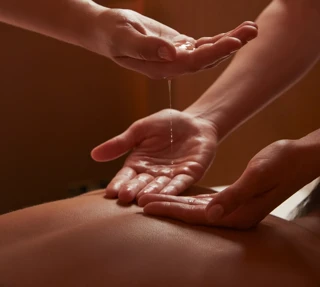 Close-up of two spa therapists pouring warm oil into hands during a treatment in softly lit, tranquil surroundings.