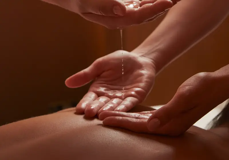 Close-up of two spa therapists pouring warm oil into hands during a treatment in softly lit, tranquil surroundings.