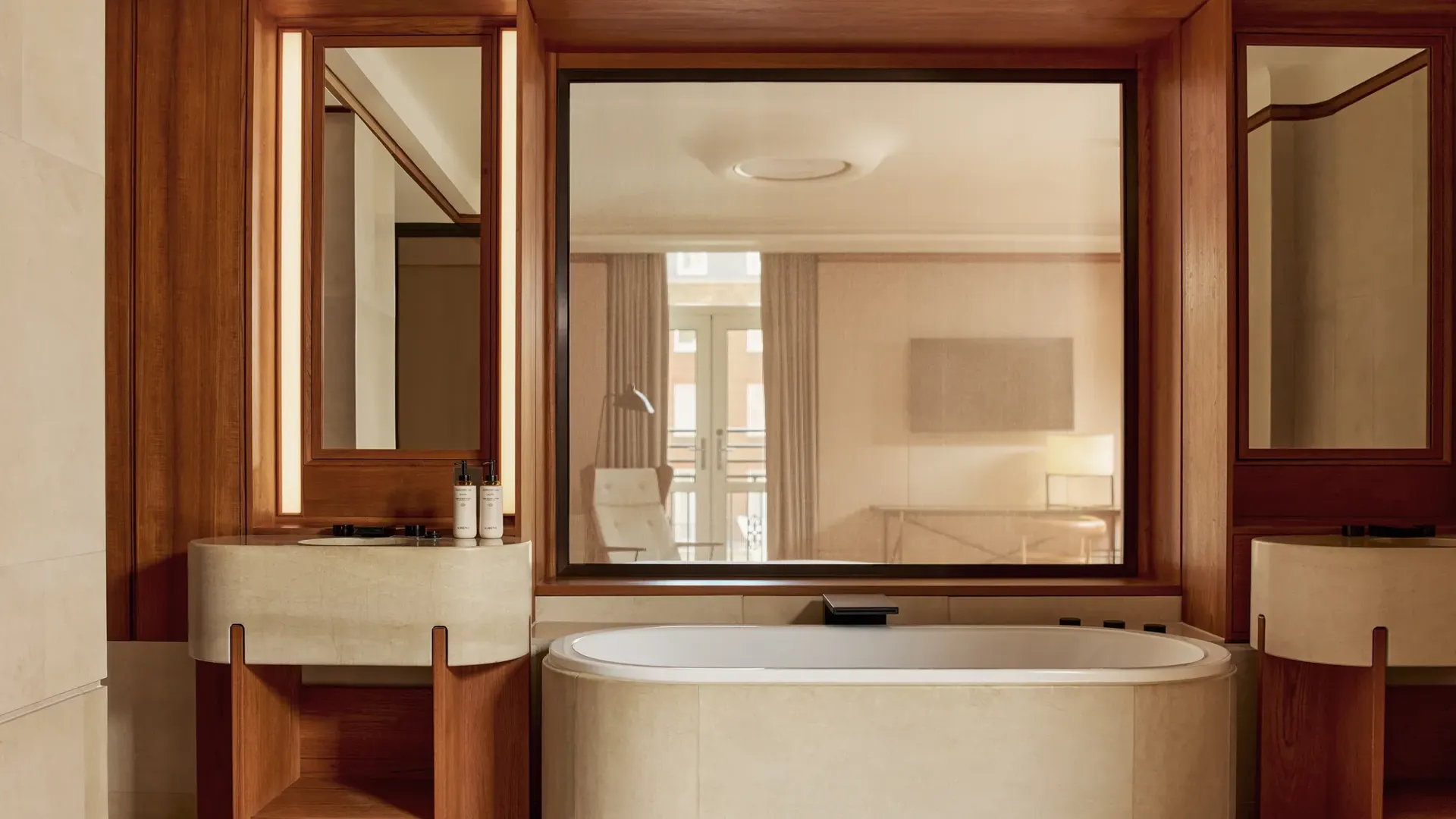 Luxurious marble bathroom in the Knightsbridge Suite with a deep soaking tub, dual vanities with wood accents, and a large window offering natural light.