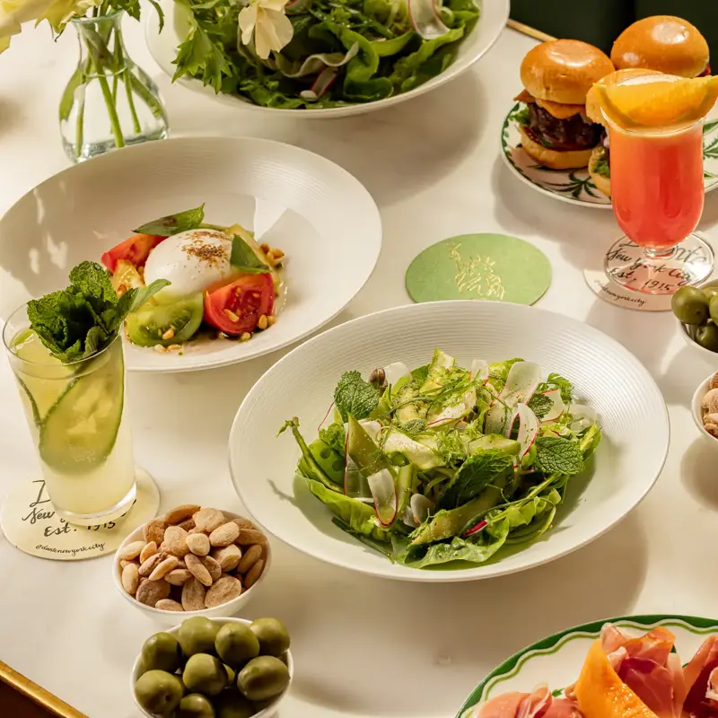 Salads, sliders, cocktails, and bar snacks arranged on an elegant marble restaurant table.