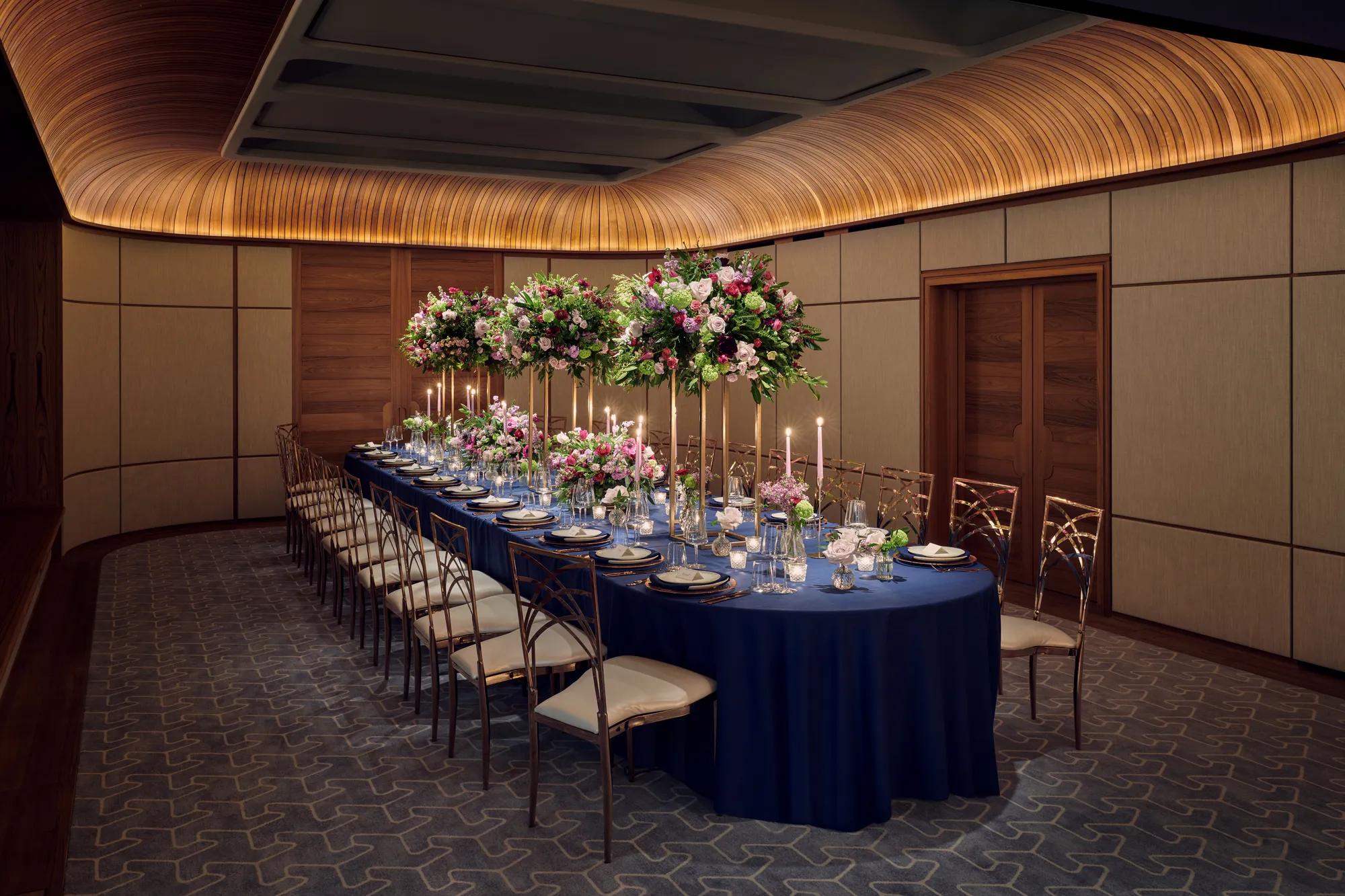 Elegant banquet table set with navy linens, tall floral centerpieces, candles, and fine glassware in a wood-panelled room