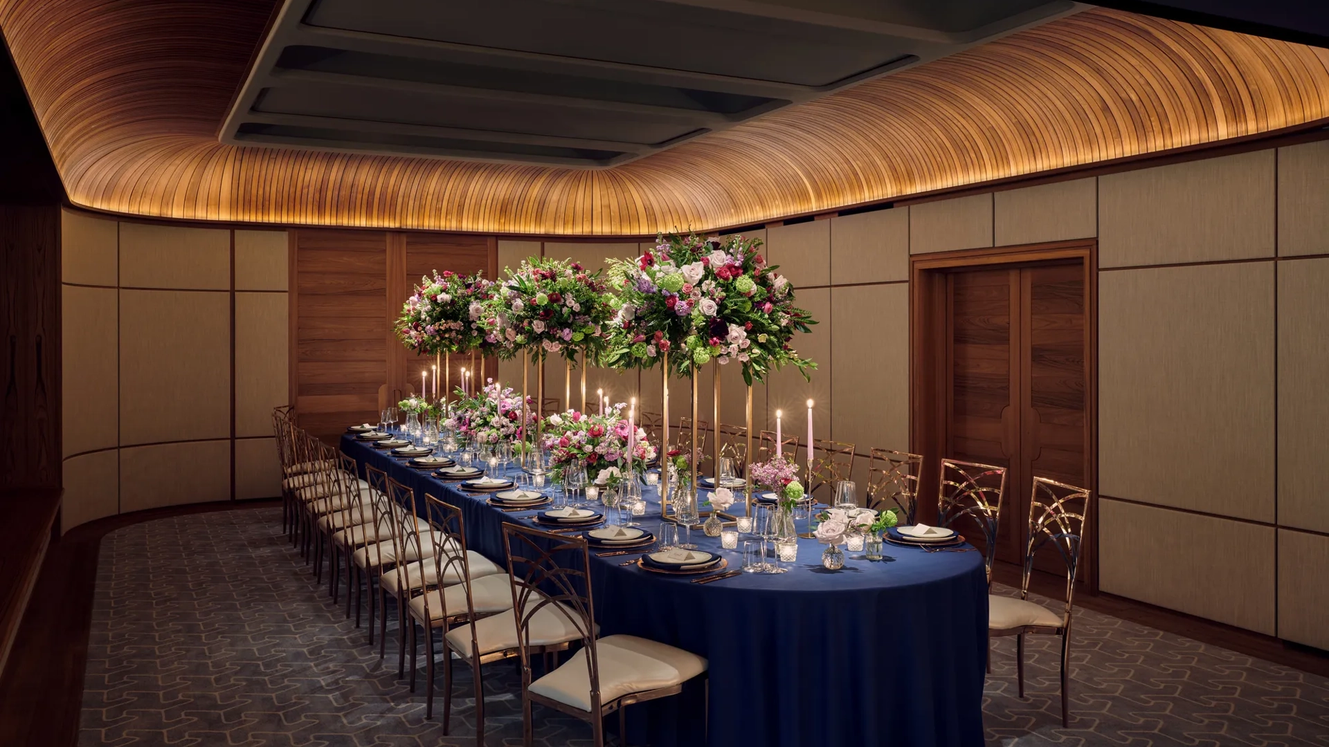 Elegant banquet table set with navy linens, tall floral centerpieces, candles, and fine glassware in a wood-panelled room