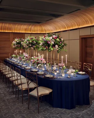 Elegant banquet table set with navy linens, tall floral centerpieces, candles, and fine glassware in a wood-panelled room