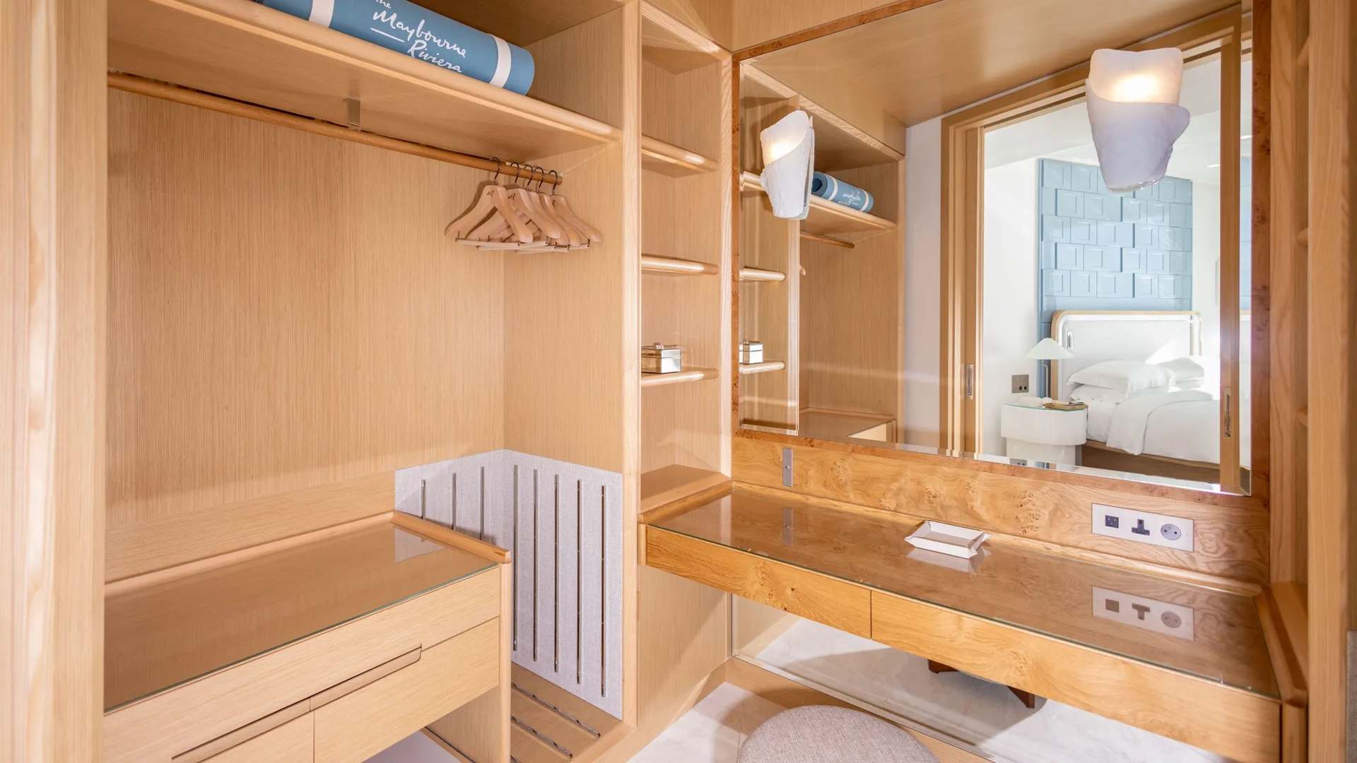Dressing moderne en bois avec étagères ouvertes, espace penderie et coiffeuse intégrée avec miroir, menant à une chambre.