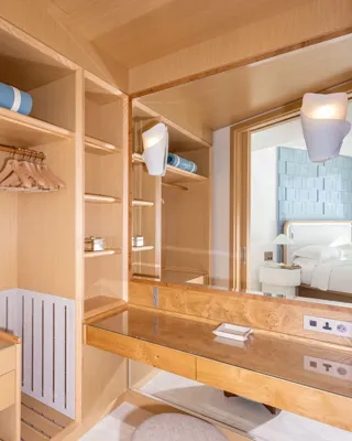 Dressing moderne en bois avec étagères ouvertes, espace penderie et coiffeuse intégrée avec miroir, menant à une chambre.