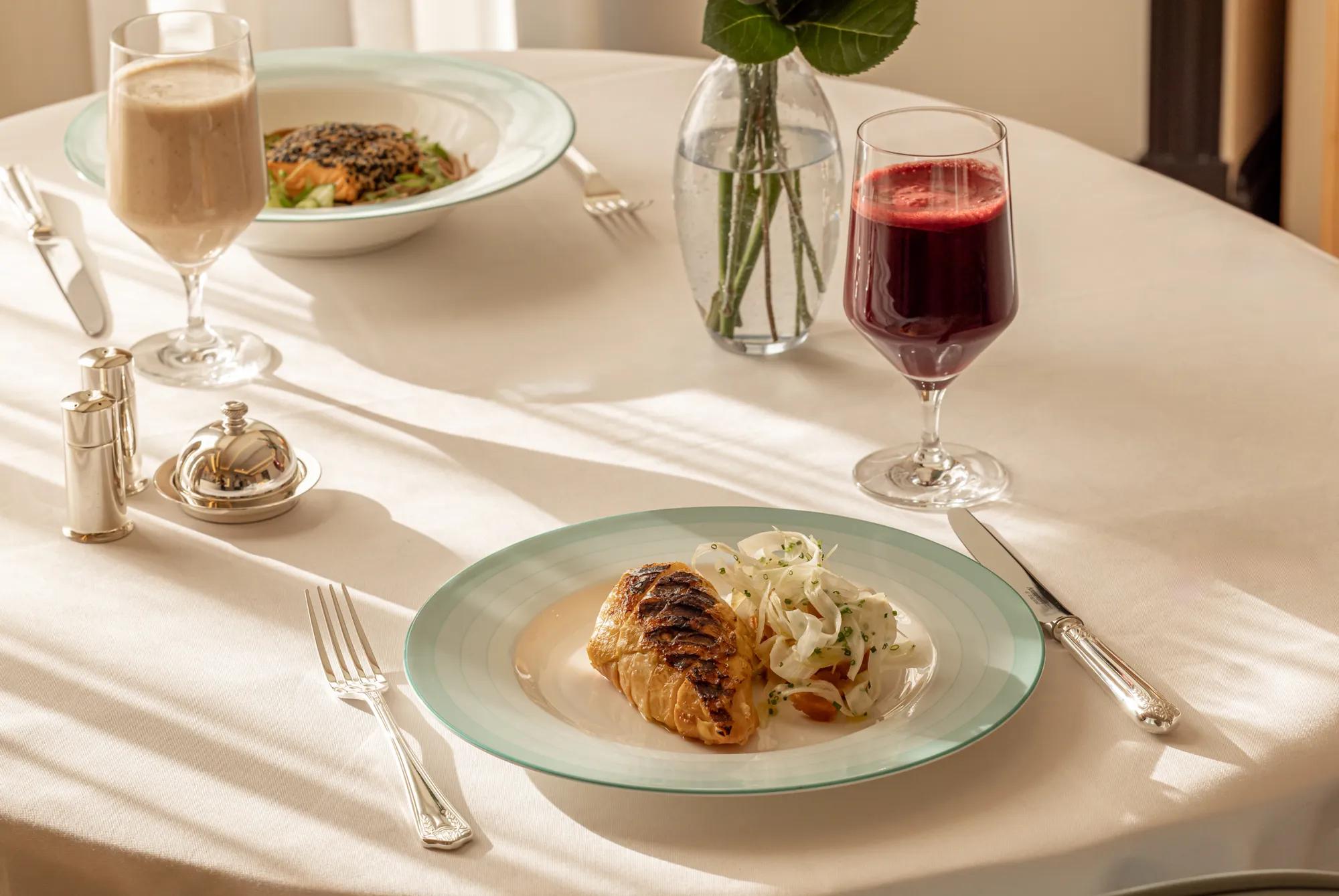 **Alt text (WCAG 2.2 AA, under 125 characters):**

Grilled fish fillet with shaved fennel salad on a white tablecloth, served with fresh juices at an elegantly set dining table.

