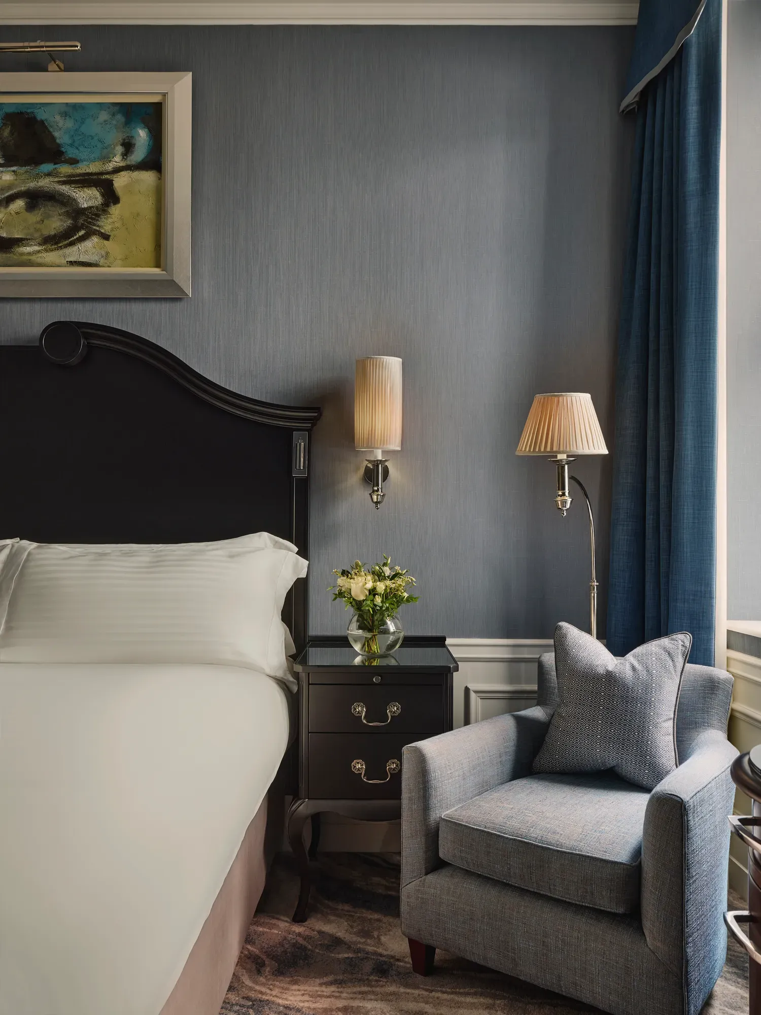Guest room corner with king bed, bedside table, armchair, and blue walls by window.
