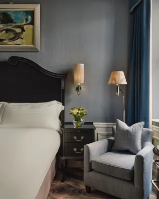 Guest room corner with king bed, bedside table, armchair, and blue walls by window.