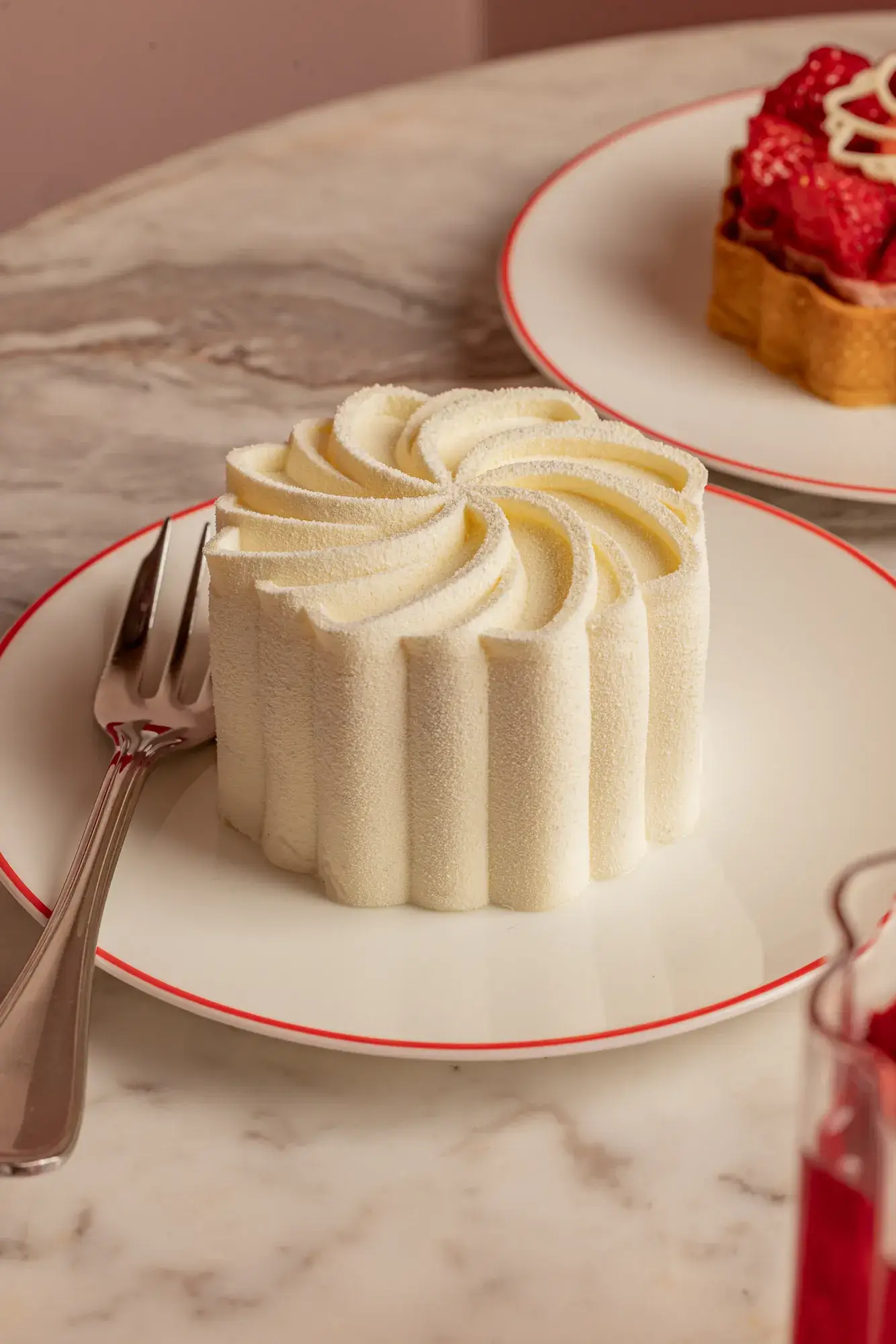 White swirled mousse dessert on a red-rimmed plate with a fork beside it on a marble table.