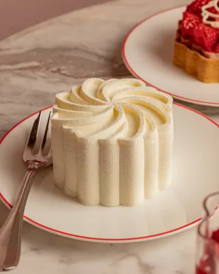 White swirled mousse dessert on a red-rimmed plate with a fork beside it on a marble table.