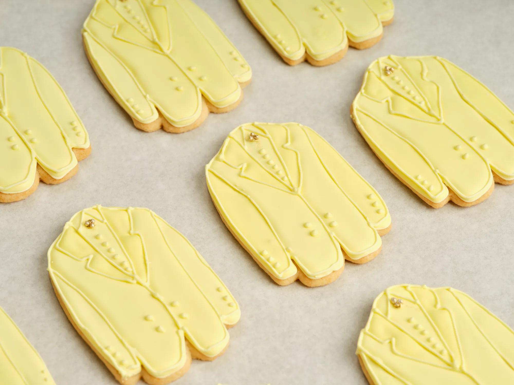 Rows of yellow suit‑shaped iced cookies arranged neatly on a baking tray.