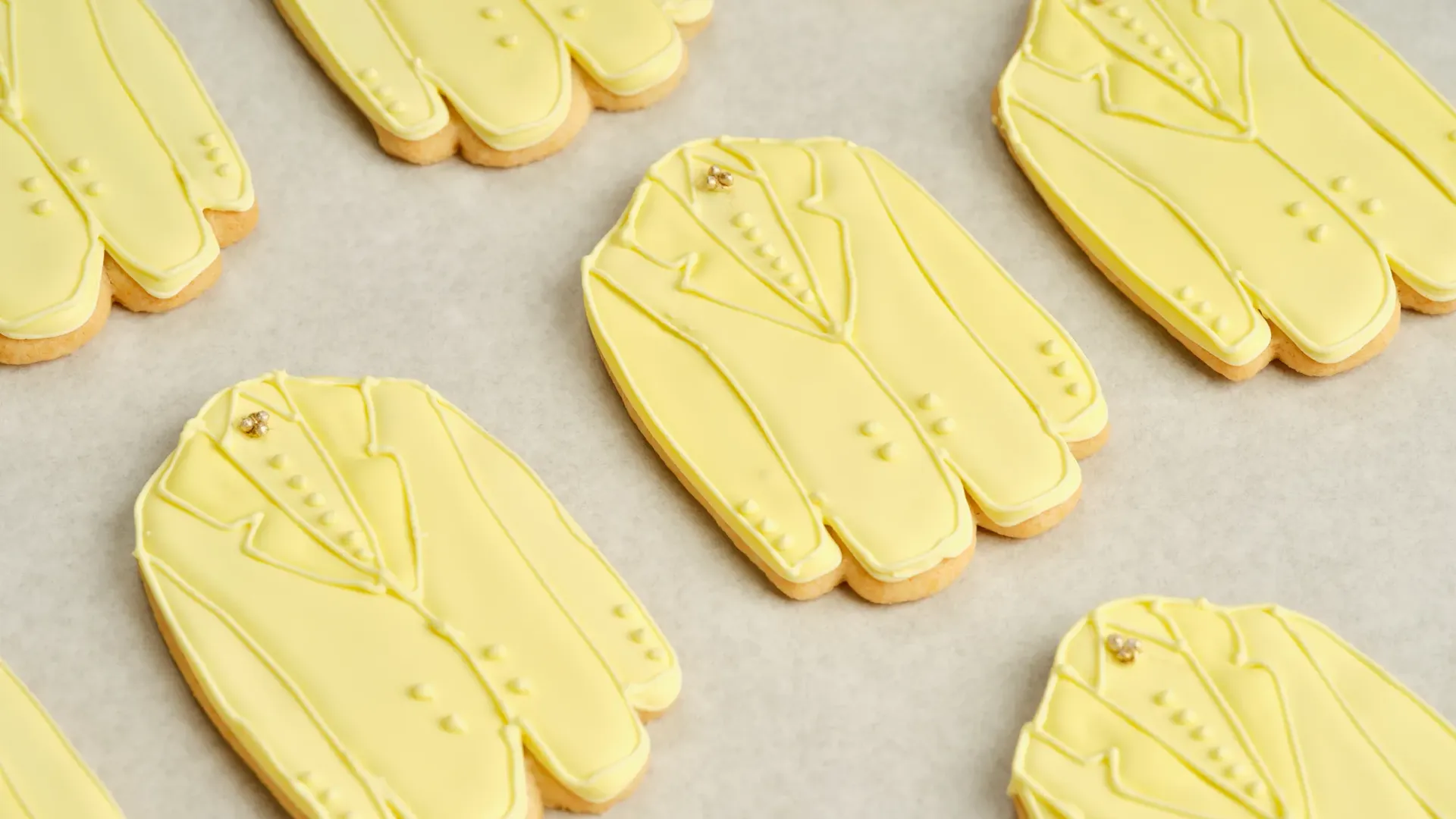 Rows of yellow suit‑shaped iced cookies arranged neatly on a baking tray.