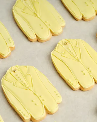 Rows of yellow suit‑shaped iced cookies arranged neatly on a baking tray.