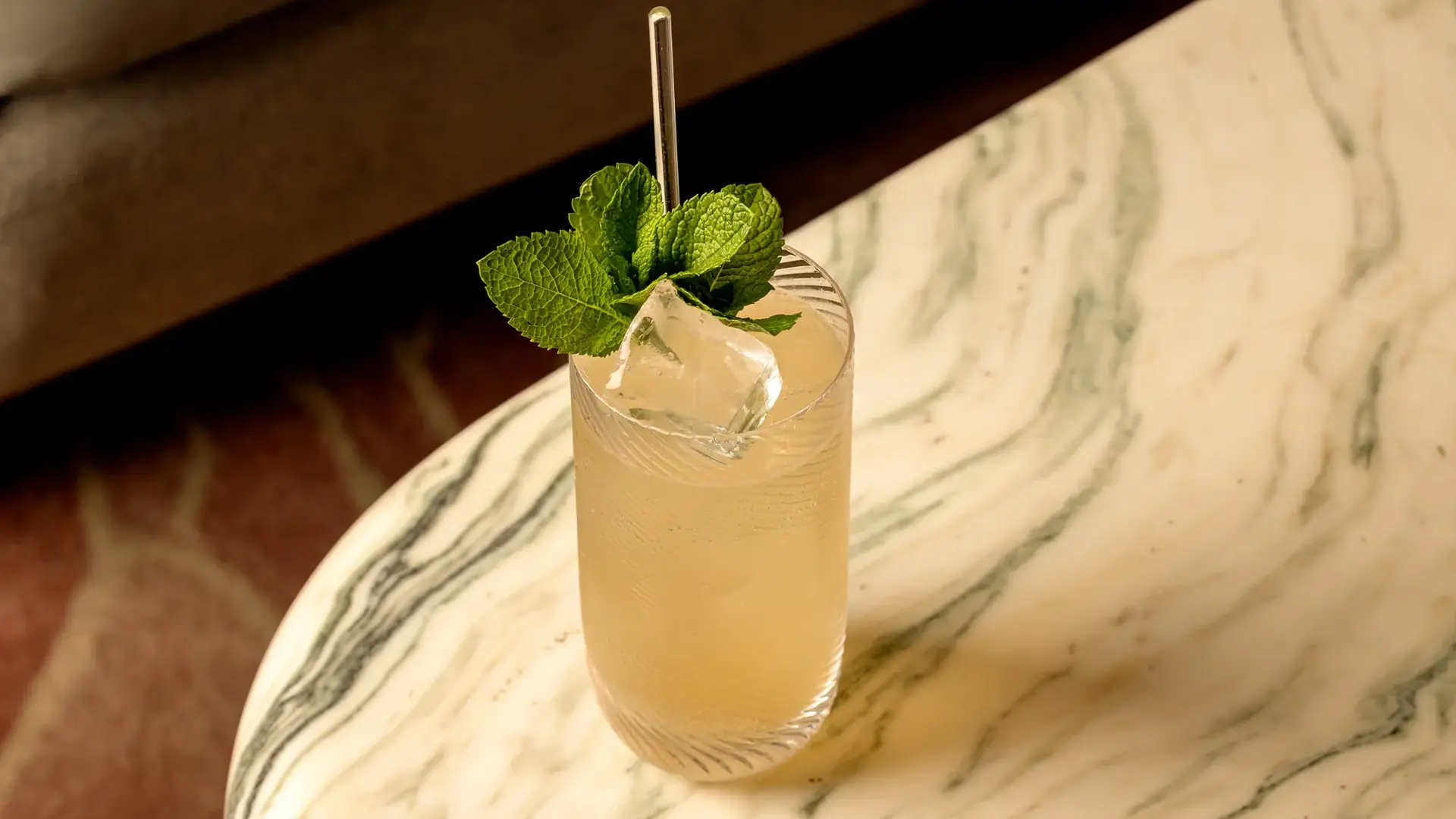 Tall iced cocktail garnished with fresh mint on a marbled table.