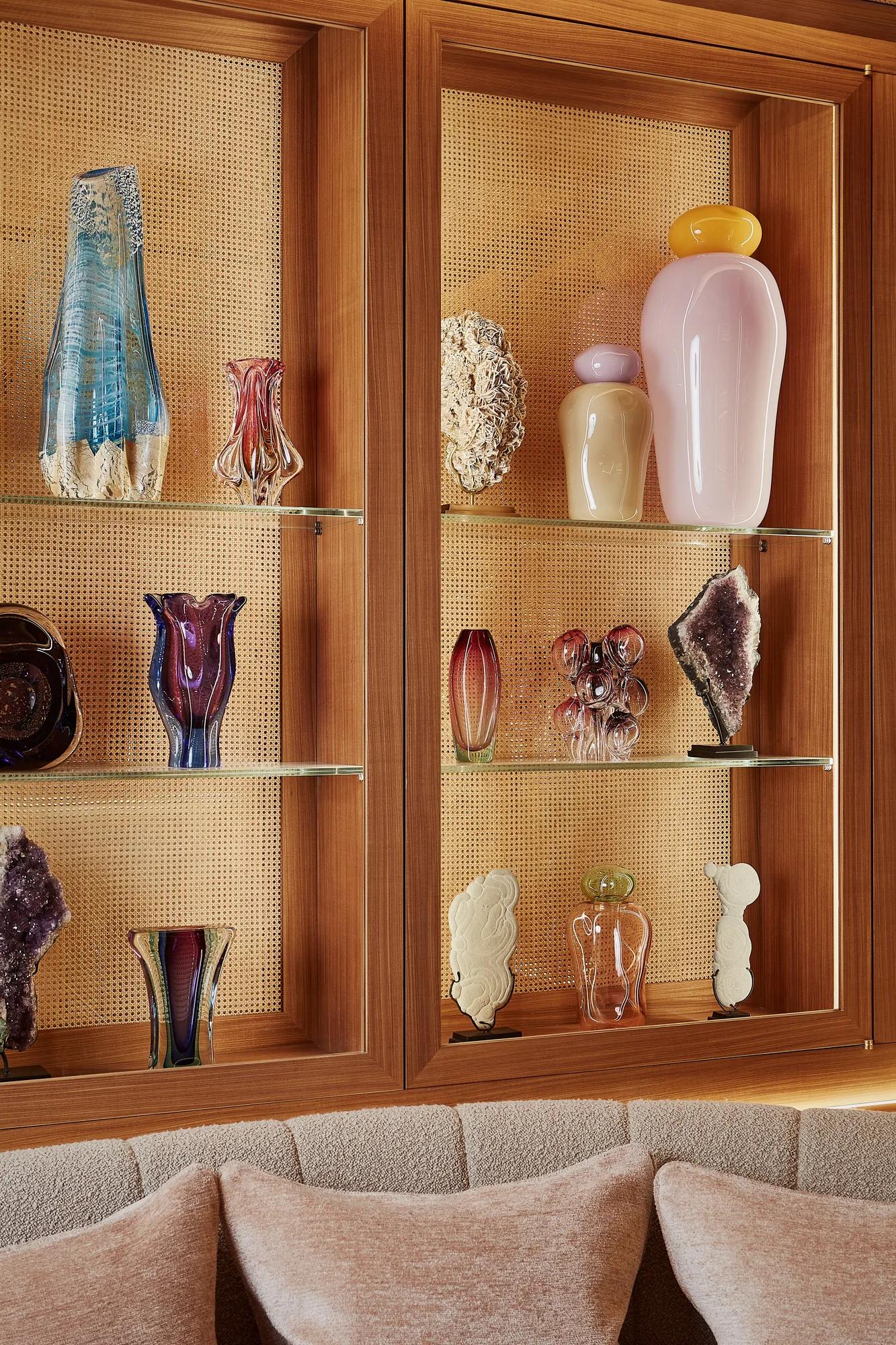 Illuminated wooden shelves displaying decorative glass vases and sculptural objects above a cushioned lounge banquette.