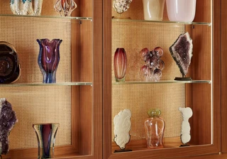 Illuminated wooden shelves displaying decorative glass vases and sculptural objects above a cushioned lounge banquette.
