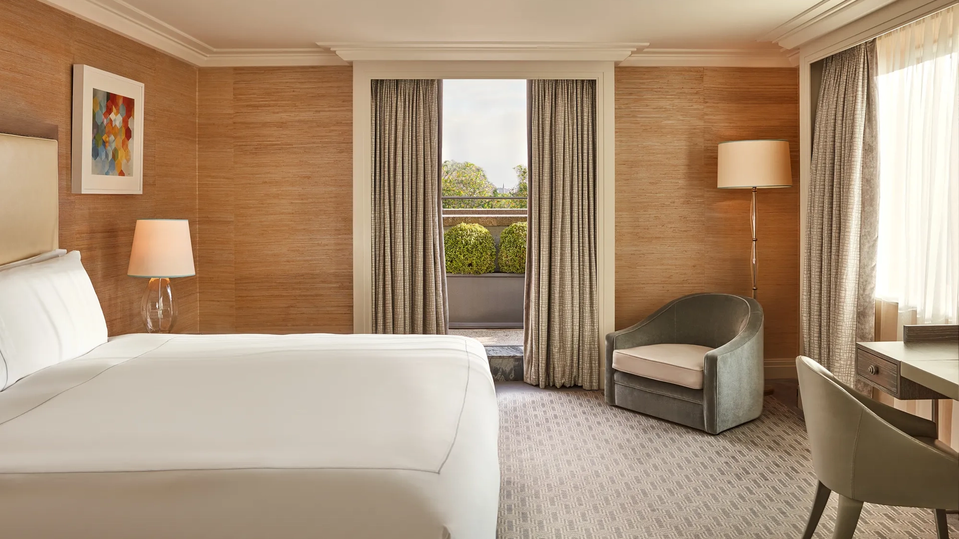 Bedroom with large bed, armchair, and French doors opening to private terrace with greenery.