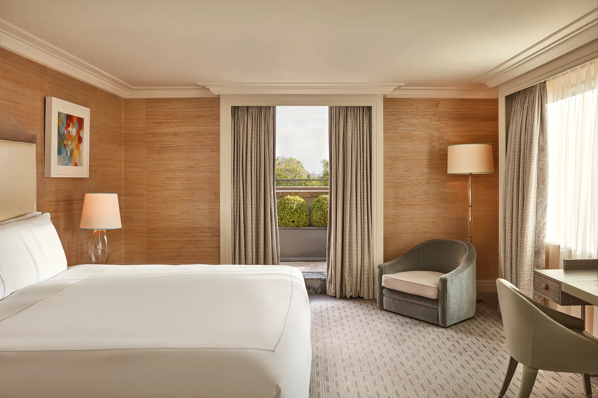 Bedroom with large bed, armchair, and French doors opening to private terrace with greenery.