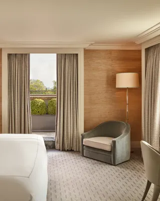 Bedroom with large bed, armchair, and French doors opening to private terrace with greenery.