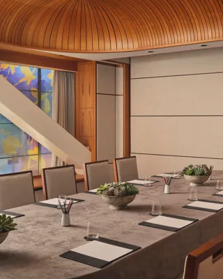 Boardroom setup with long table, notepads, succulents, and patterned glass window under curved wood ceiling.