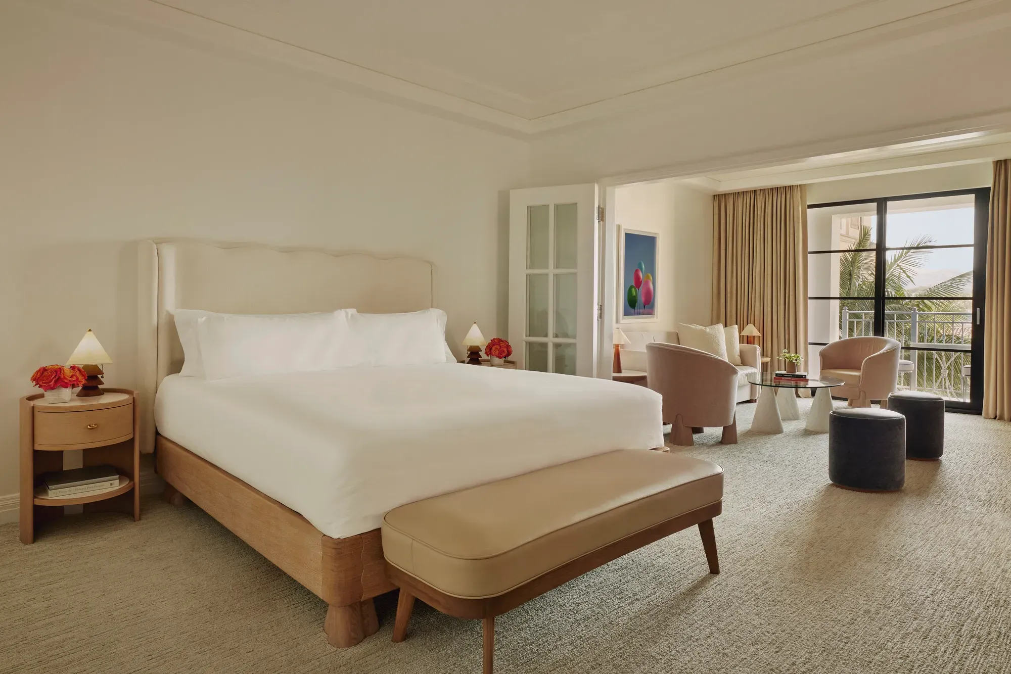 Junior suite with king bed and bench leading to a separate sitting area through French doors, opening to a balcony with palm views.
