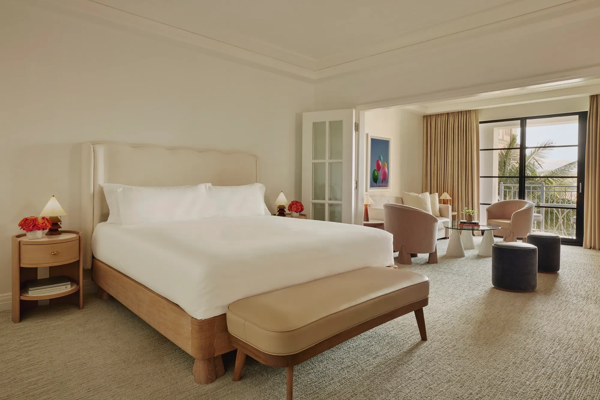 Junior suite with king bed and bench leading to a separate sitting area through French doors, opening to a balcony with palm views.