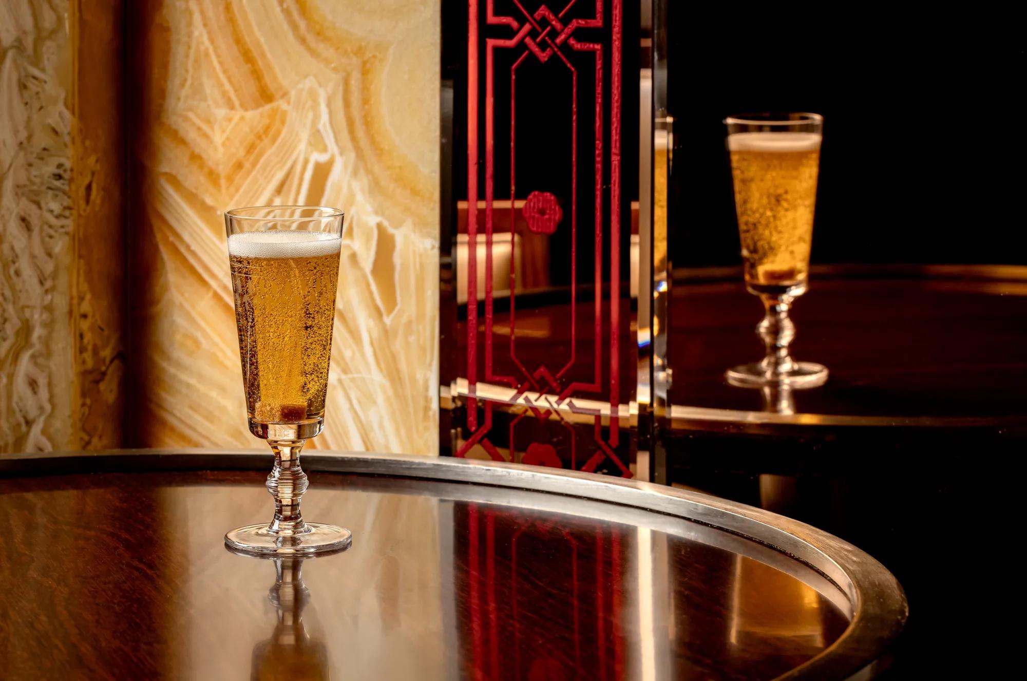 Glass of sparkling beer on a polished bar table with mirrored reflection in an art deco setting.