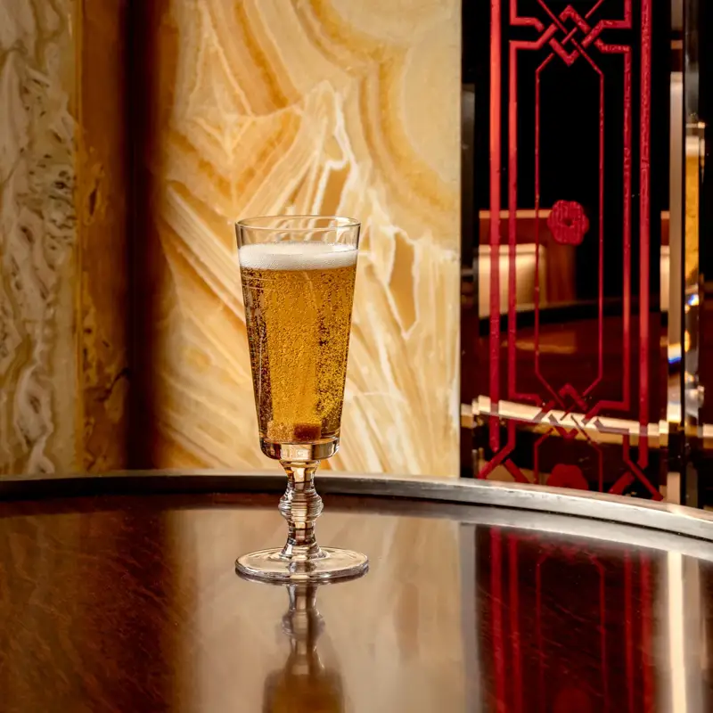 Glass of sparkling beer on a polished bar table with mirrored reflection in an art deco setting.