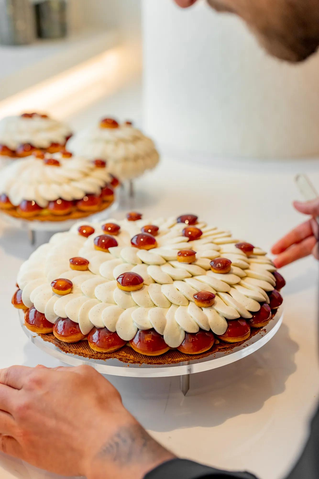A pastry chef adds finishing touches to a Cédric Grolet tart topped with piped cream petals and glossy caramelised domes.