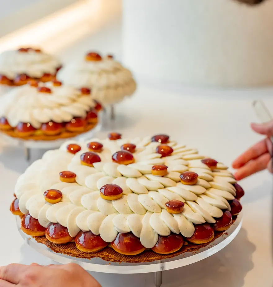 A pastry chef adds finishing touches to a Cédric Grolet tart topped with piped cream petals and glossy caramelised domes.