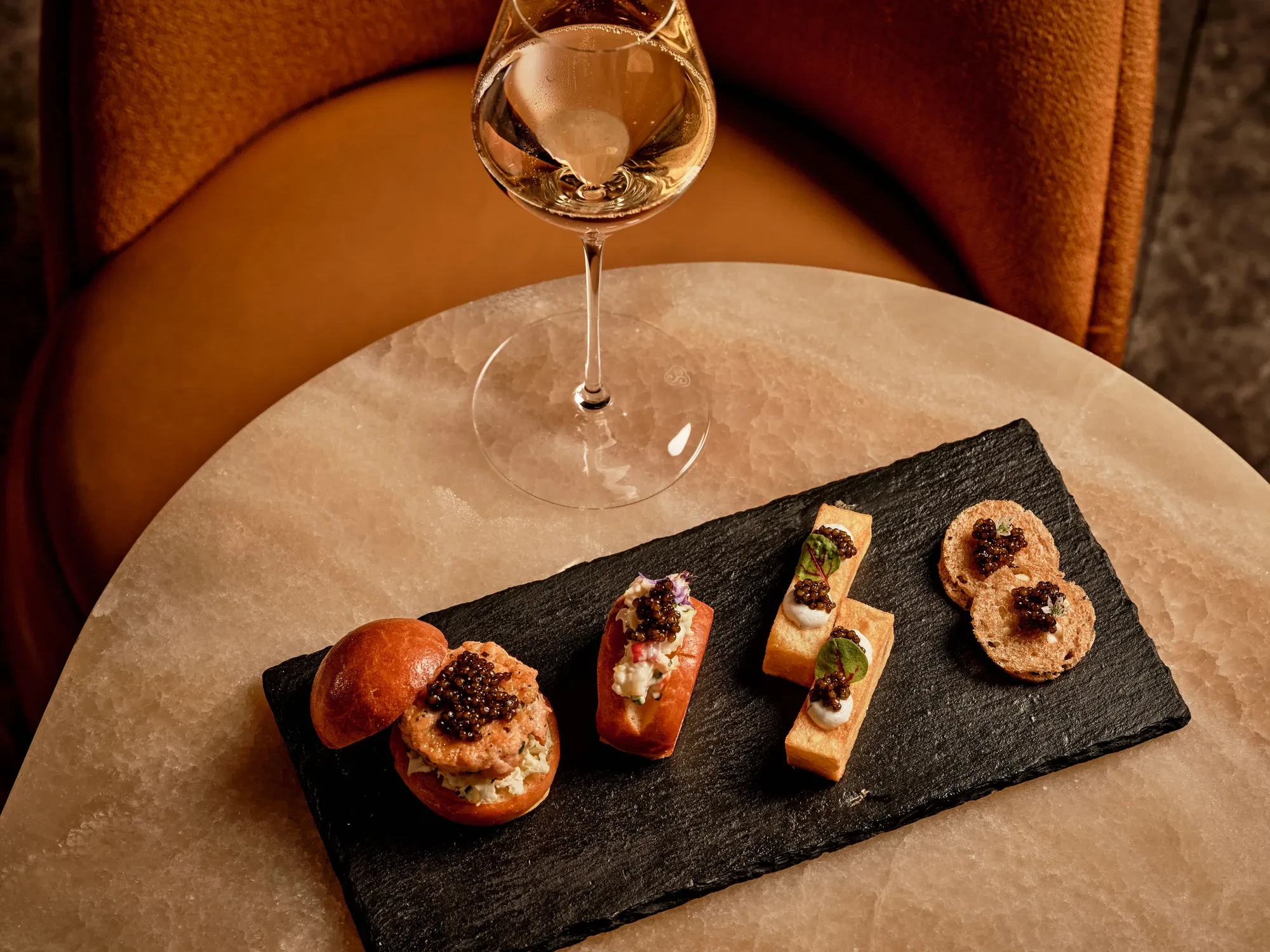 Glass of champagne served with caviar tin, potato chips, and crème fraîche at Maybourne Beverly Hills.