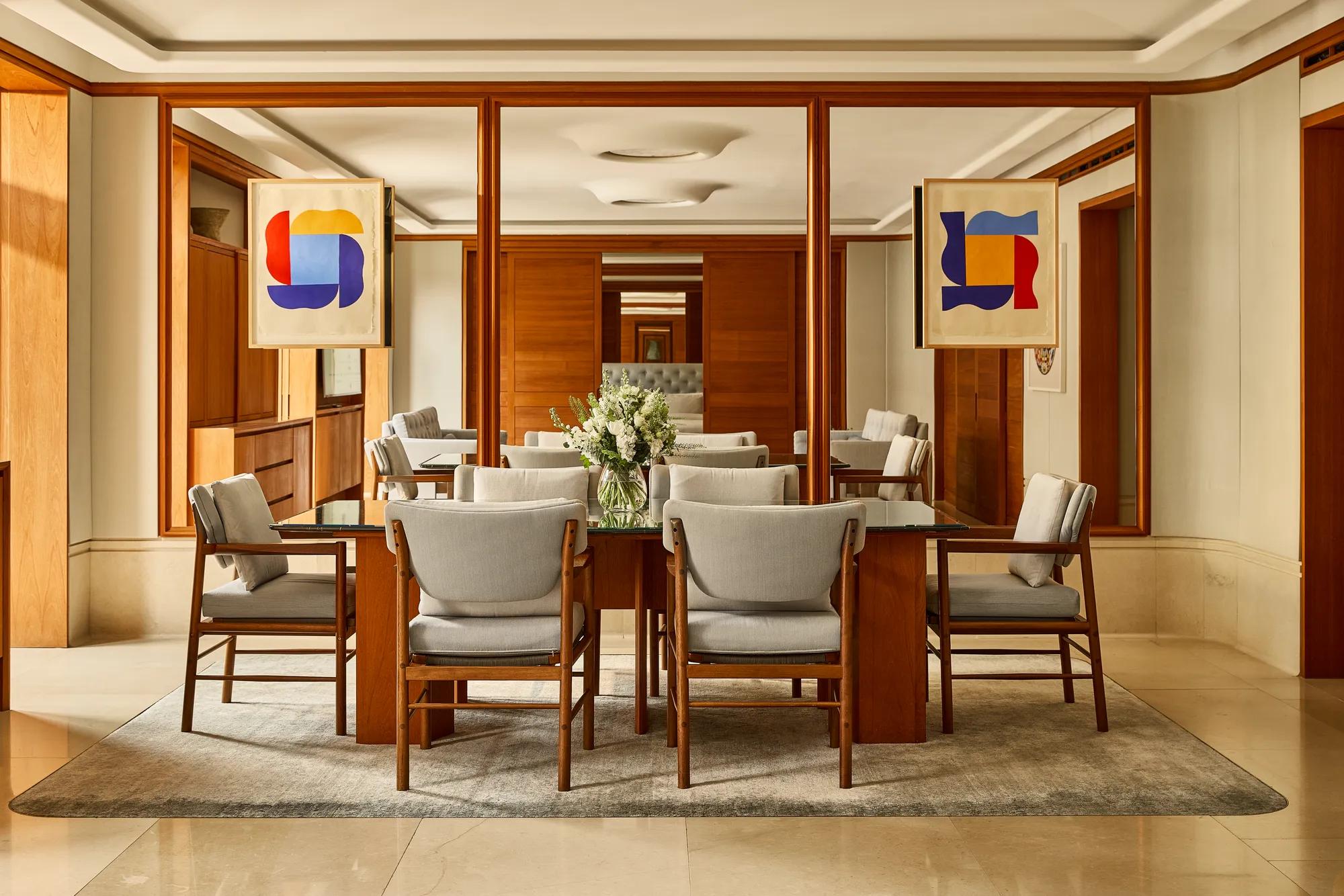 Dining area with a glass-topped table for six, upholstered chairs, floral arrangement, and mirrored walls framed by warm wood panelling.
