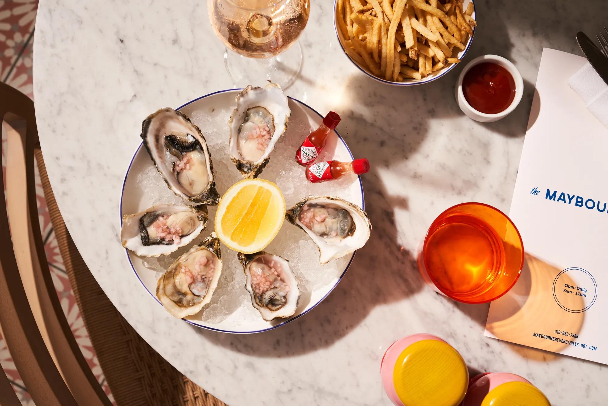 Plate of oysters with lemon, fries, ketchup, and a glass of wine on a marble table.