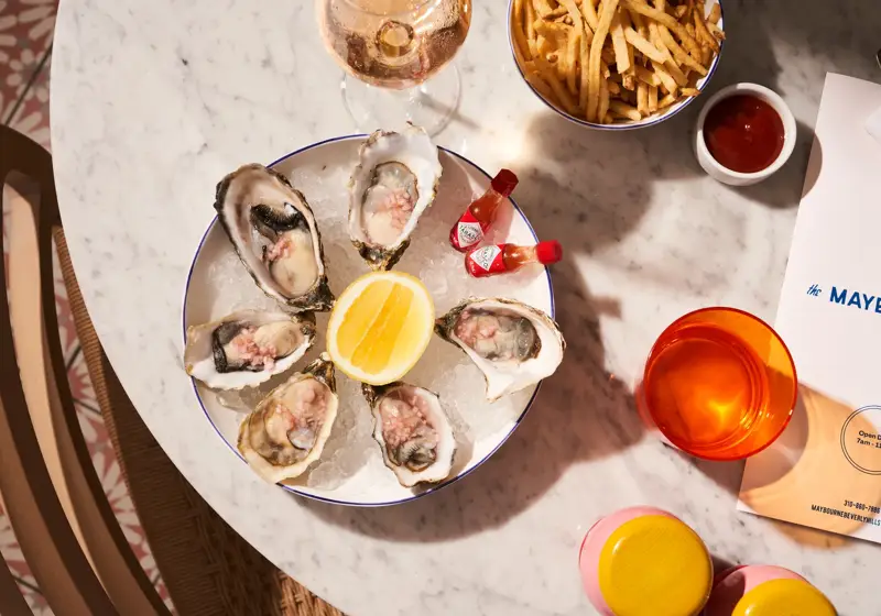 Plate of oysters with lemon, fries, ketchup, and a glass of wine on a marble table.