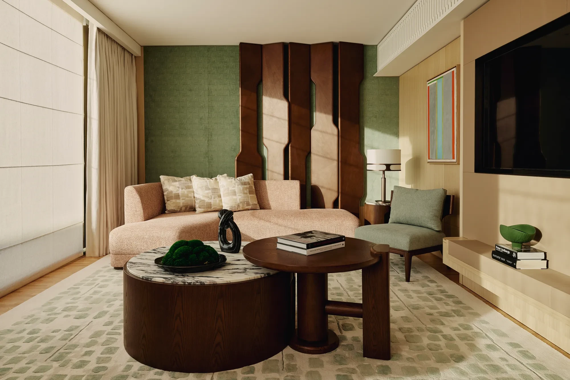 Stylish suite lounge with curved pink sofa, sculptural wall panel, and dual round coffee tables on green-patterned rug.