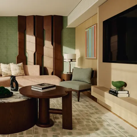Stylish suite lounge with curved pink sofa, sculptural wall panel, and dual round coffee tables on green-patterned rug.