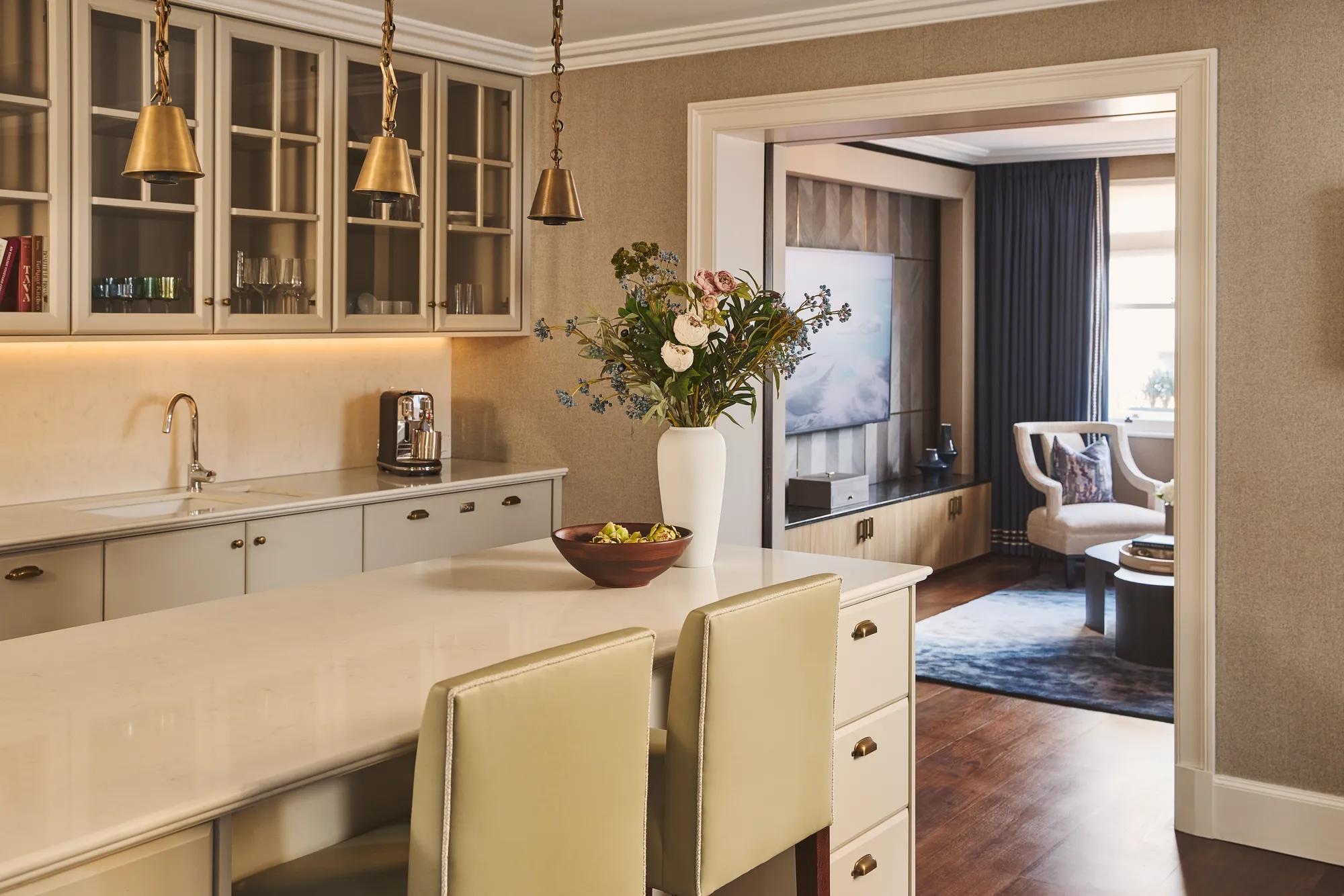 Bright kitchen island with pendant lights and flowers, leading into a cosy living area with seating and TV.