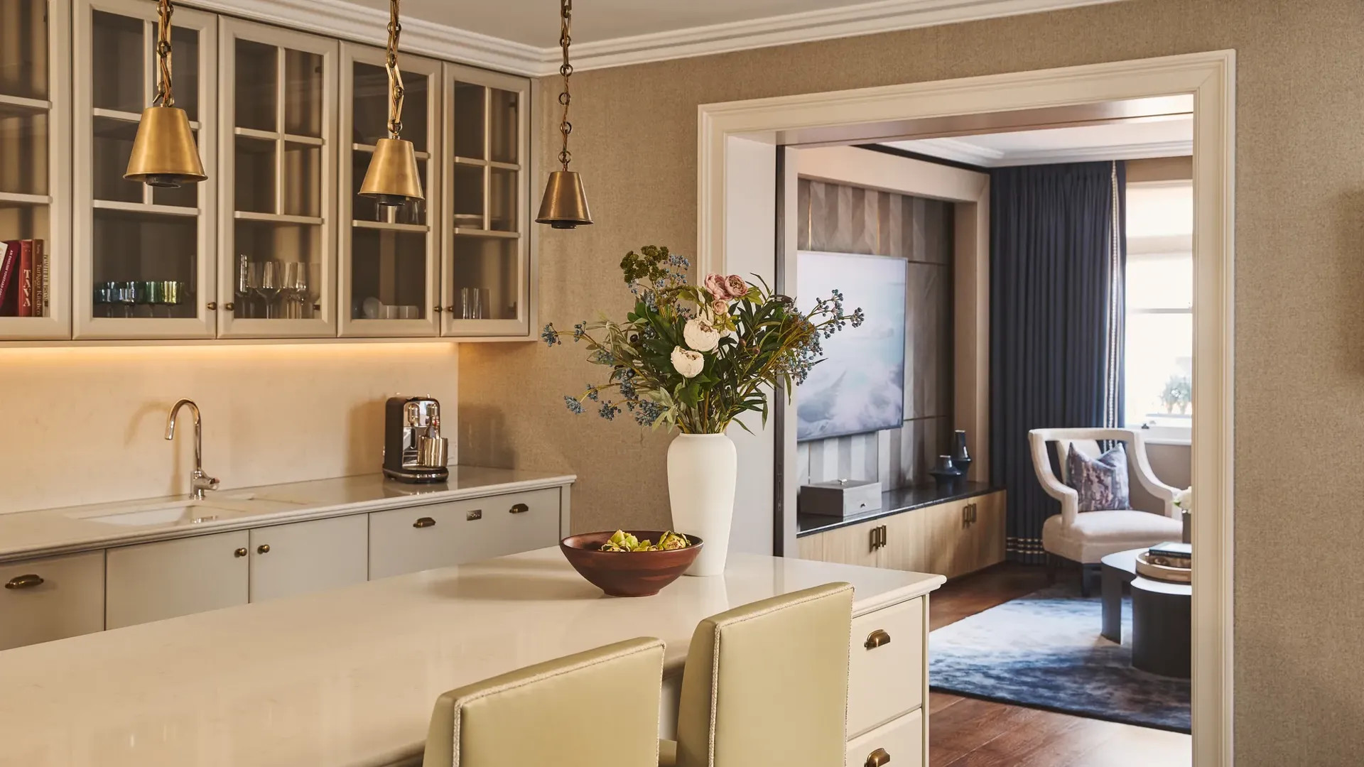 Bright kitchen island with pendant lights and flowers, leading into a cosy living area with seating and TV.