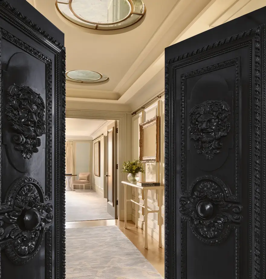 Ornate black double doors open to an elegant hallway with console table and ceiling skylights.