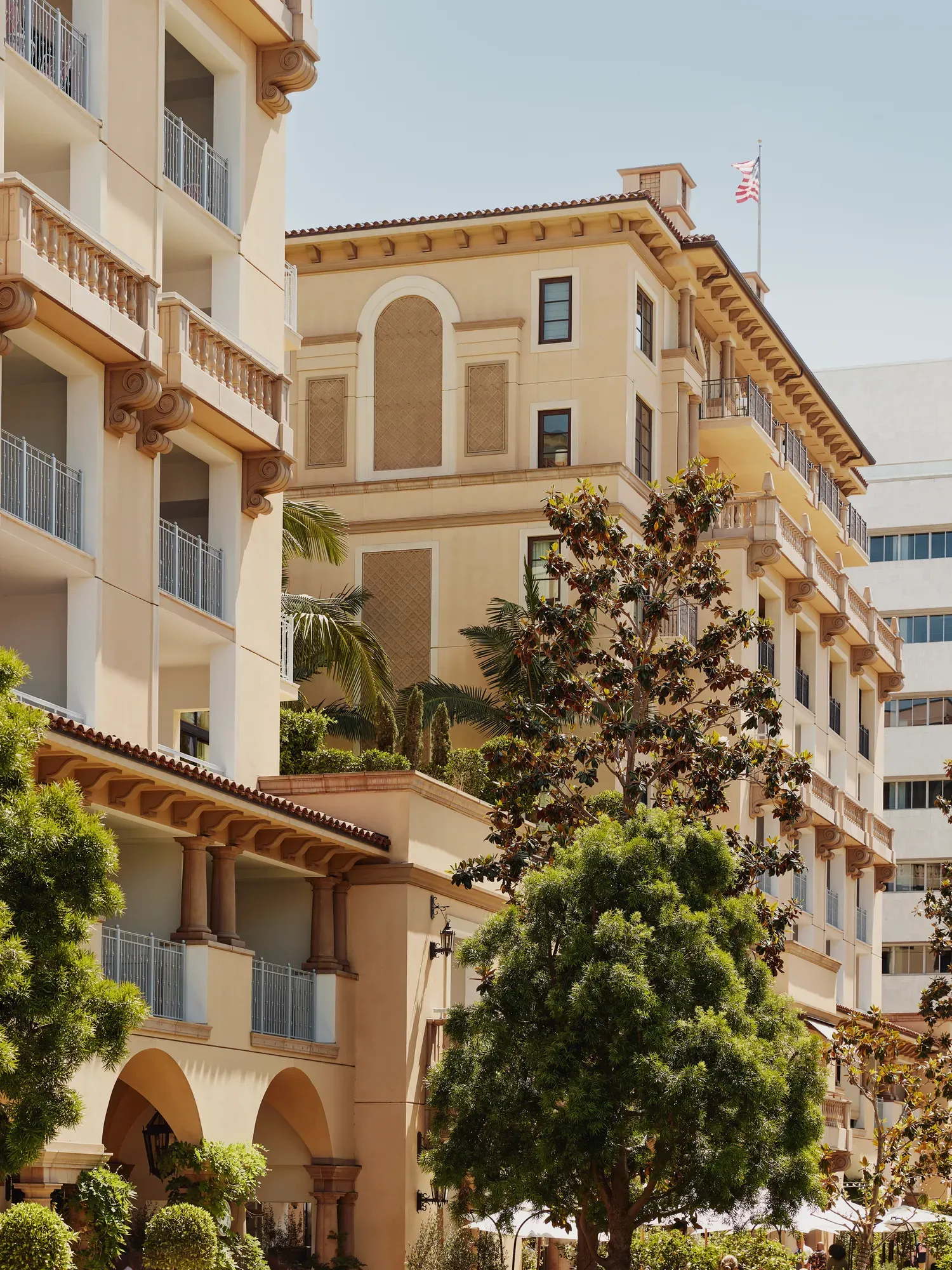 Mediterranean-style hotel façade with balconies and arches framed by magnolia trees.