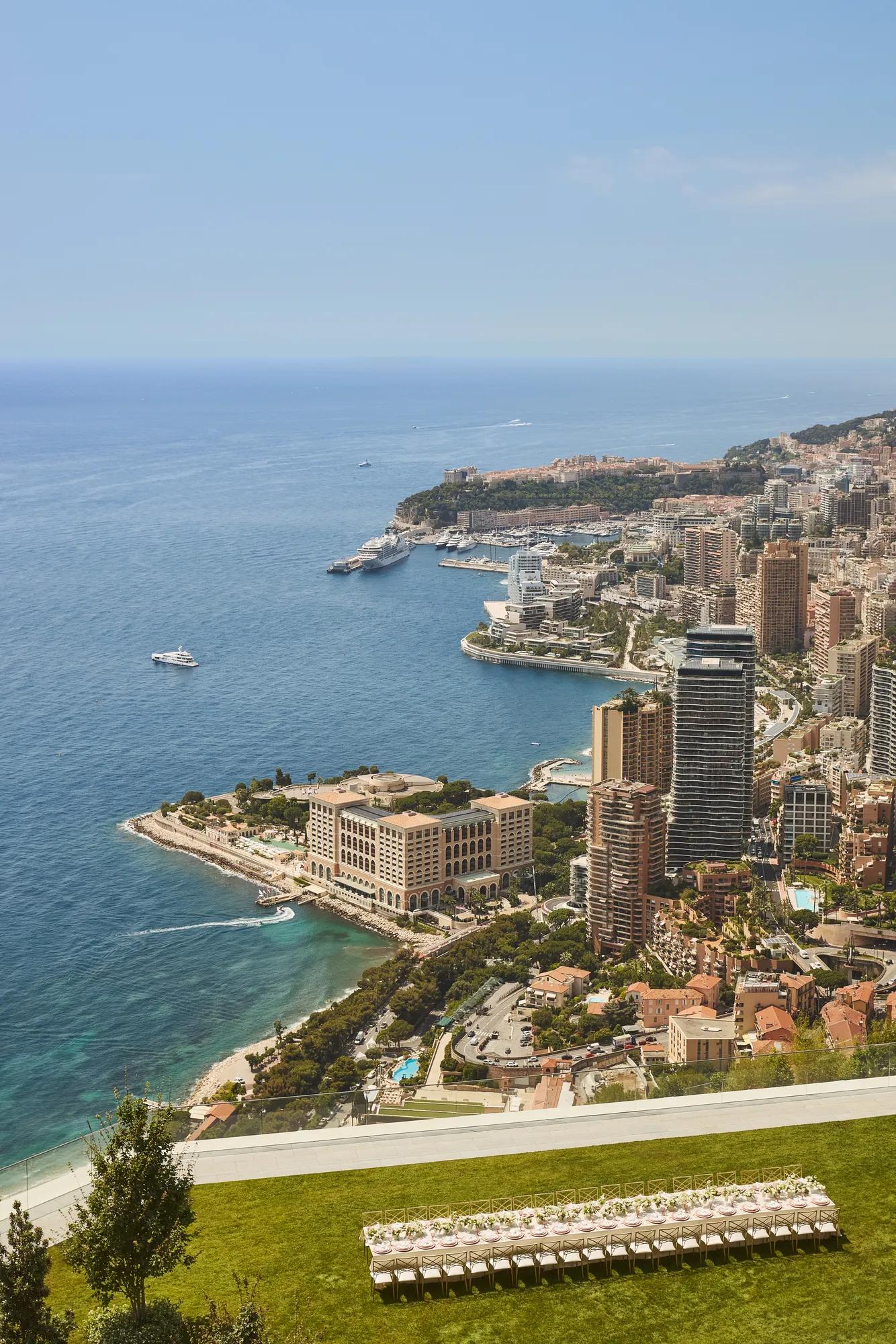 Vue panoramique du littoral de Monaco avec immeubles, yachts en mer et terrasse herbeuse au premier plan.