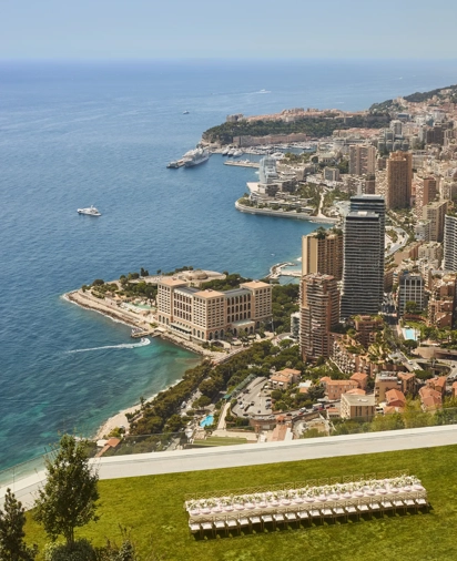 Vue panoramique du littoral de Monaco avec immeubles, yachts en mer et terrasse herbeuse au premier plan.
