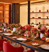 Vibrant private dining room at Claridge’s with a long wooden table set with red chairs, striped plates, and abundant floral centrepieces in red and pink hues.
