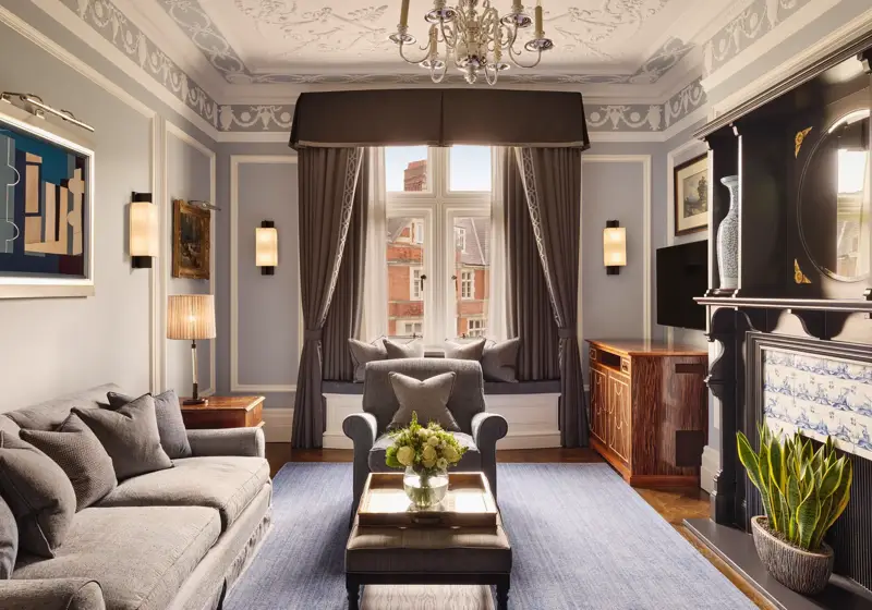 Elegant living room with grey sofa and armchairs, fireplace, window seat with cushions, and large window with drapes.