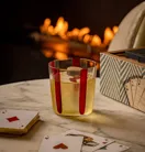 Glass of sparkling drink beside playing cards on a marble table, with a softly glowing fireplace blurred in the background.